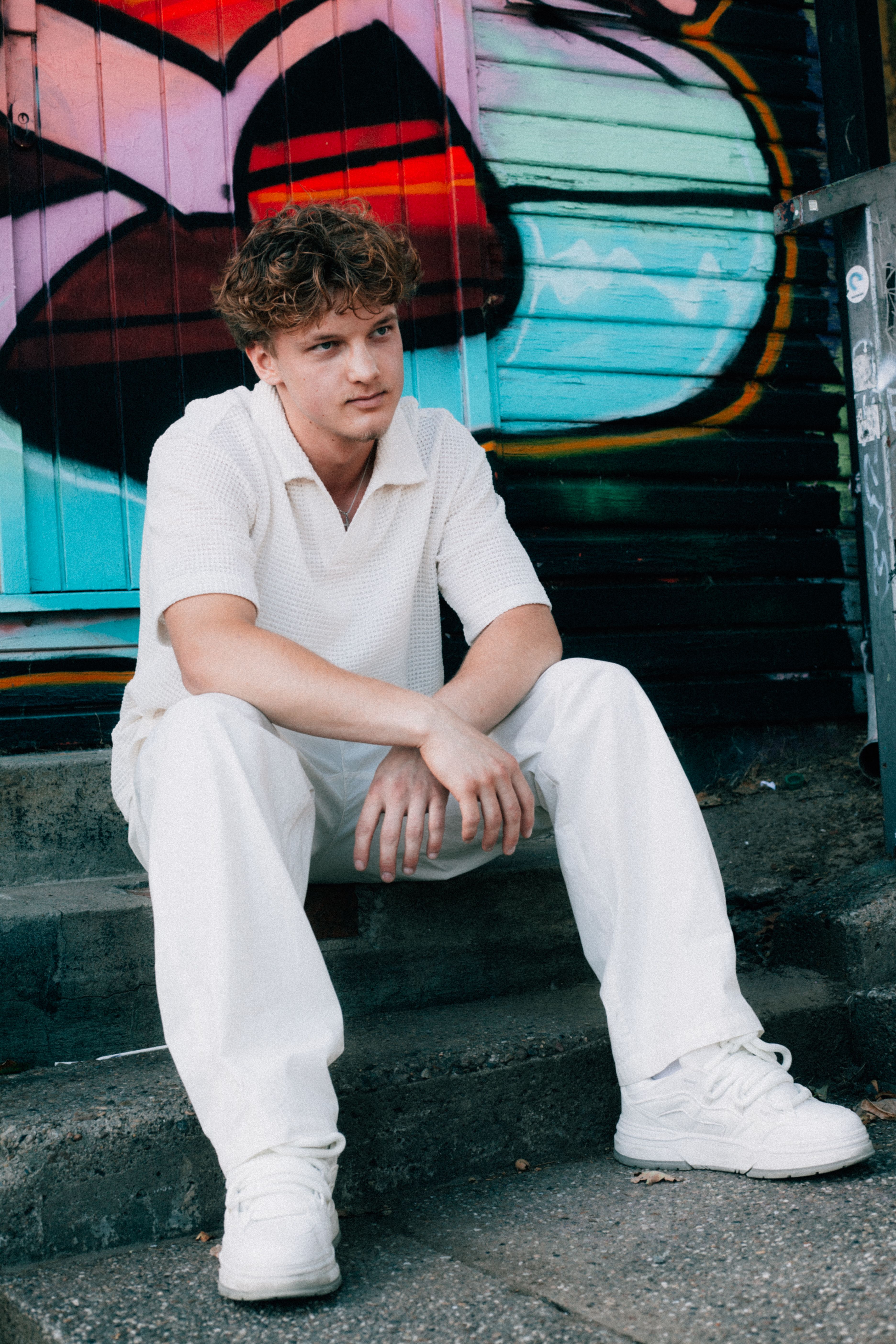 Casually dressed young adult seated on steps against a vibrant graffiti backdrop, showcasing modern urban style.