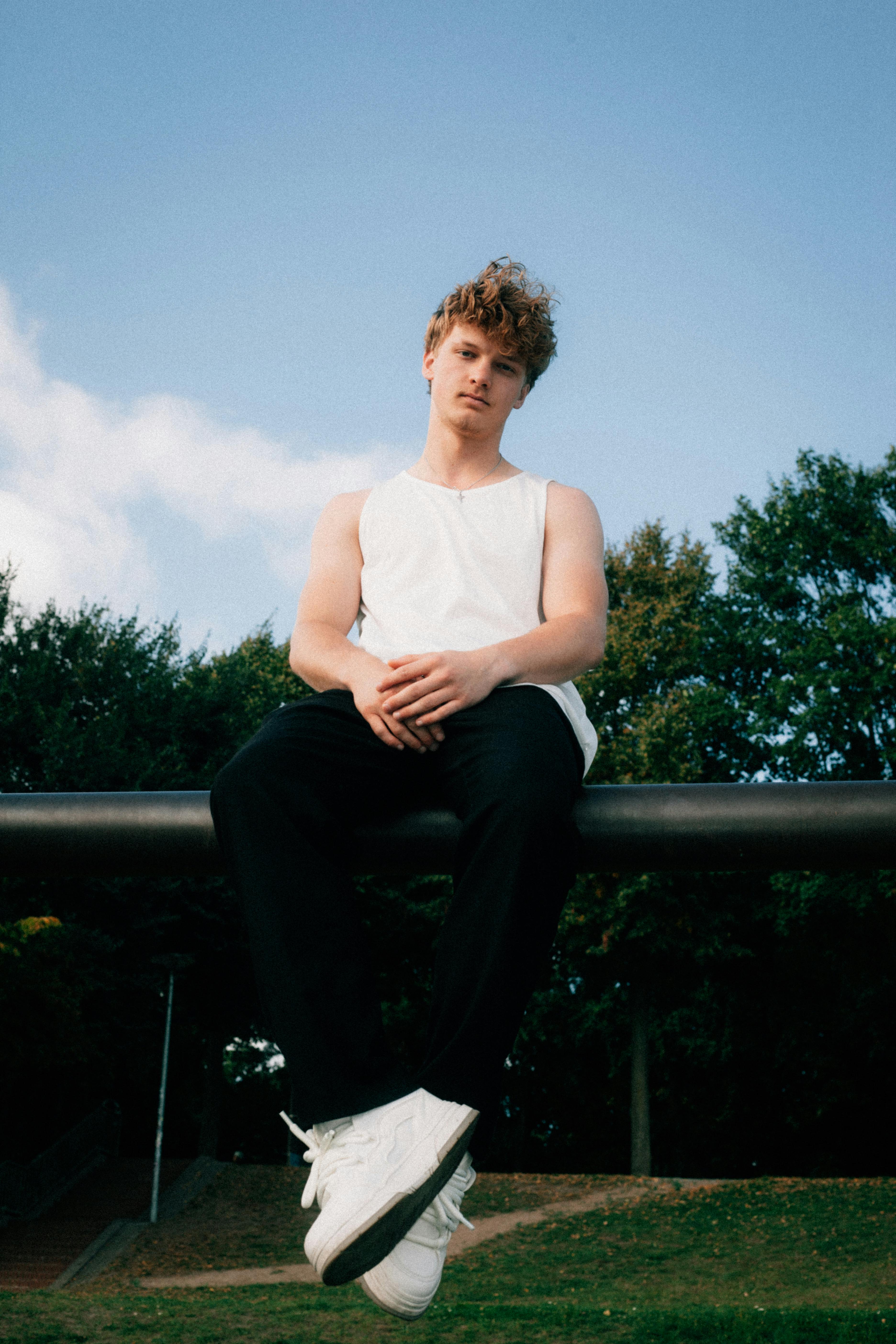 Young man in casual attire sitting outdoors on a warm summer day, reflecting modern lifestyle.