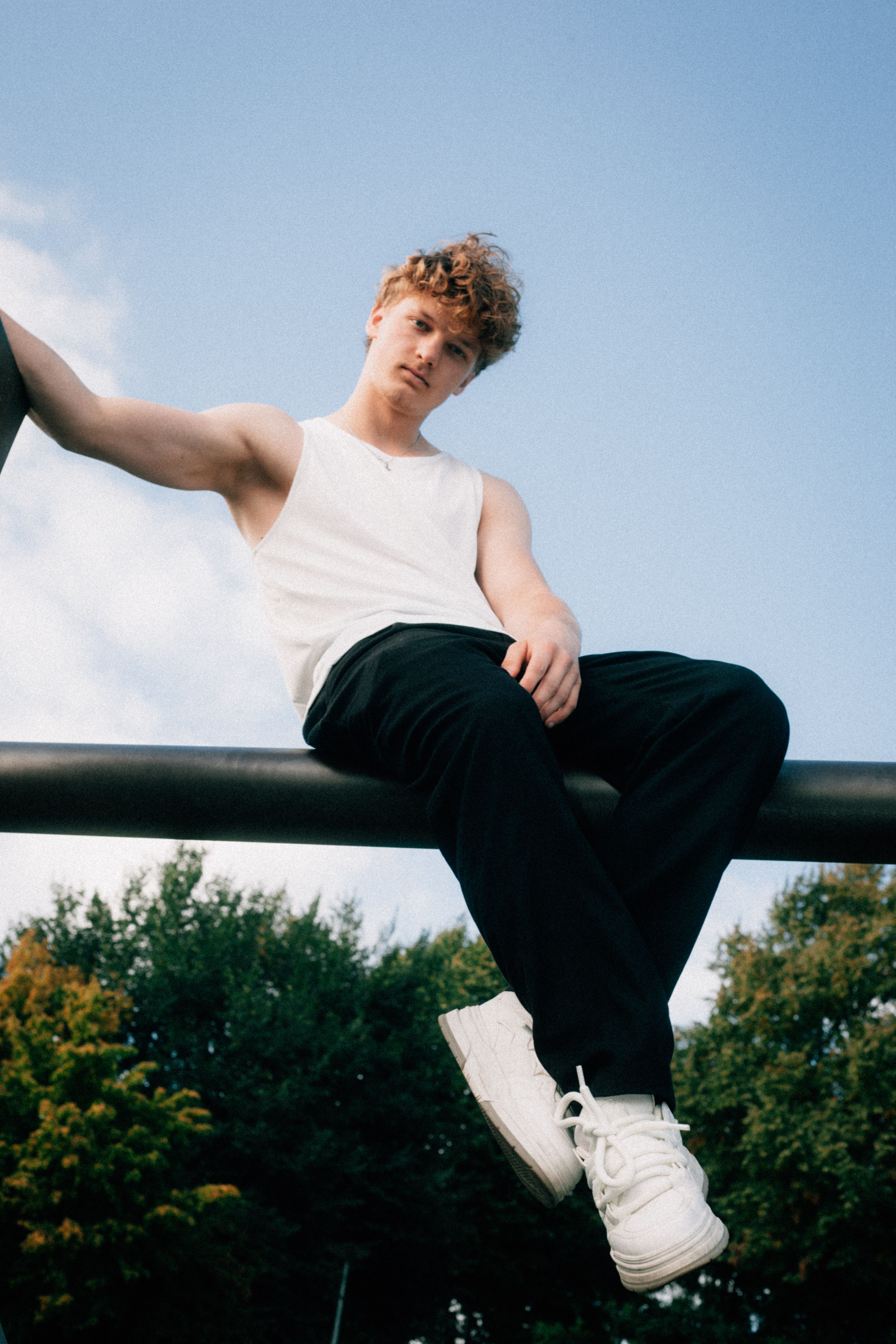 Casual portrait of a young man sitting outdoors against a blue sky, conveying a relaxed vibe.