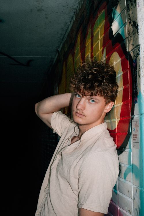 Free Stylish portrait of a young adult male standing by an urban graffiti wall, exuding a moody and artistic vibe. Stock Photo