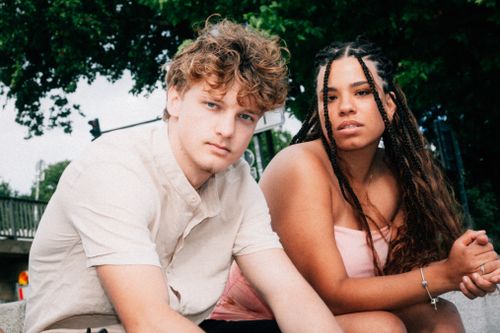 Free Two friends sitting outdoors on a sunny day, showcasing diverse fashion styles and casual summer vibes. Stock Photo