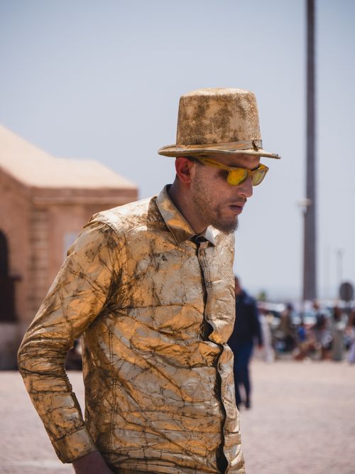 Free A person dressed in a golden outfit performs on the streets of Essaouira, Morocco, exuding a unique street art vibe. Stock Photo