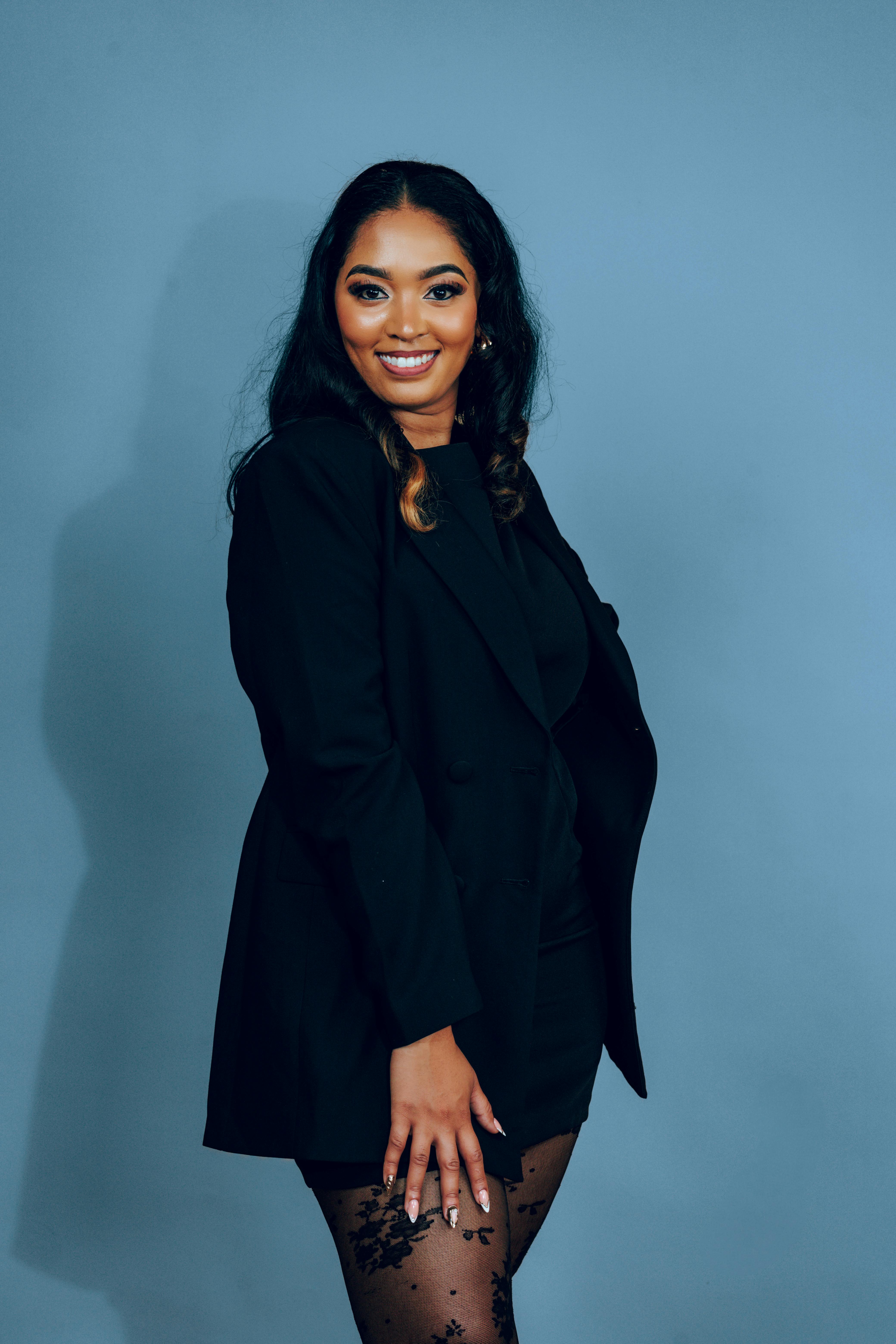 Free Stylish woman posing in a black dress and lace tights against a blue backdrop. Stock Photo