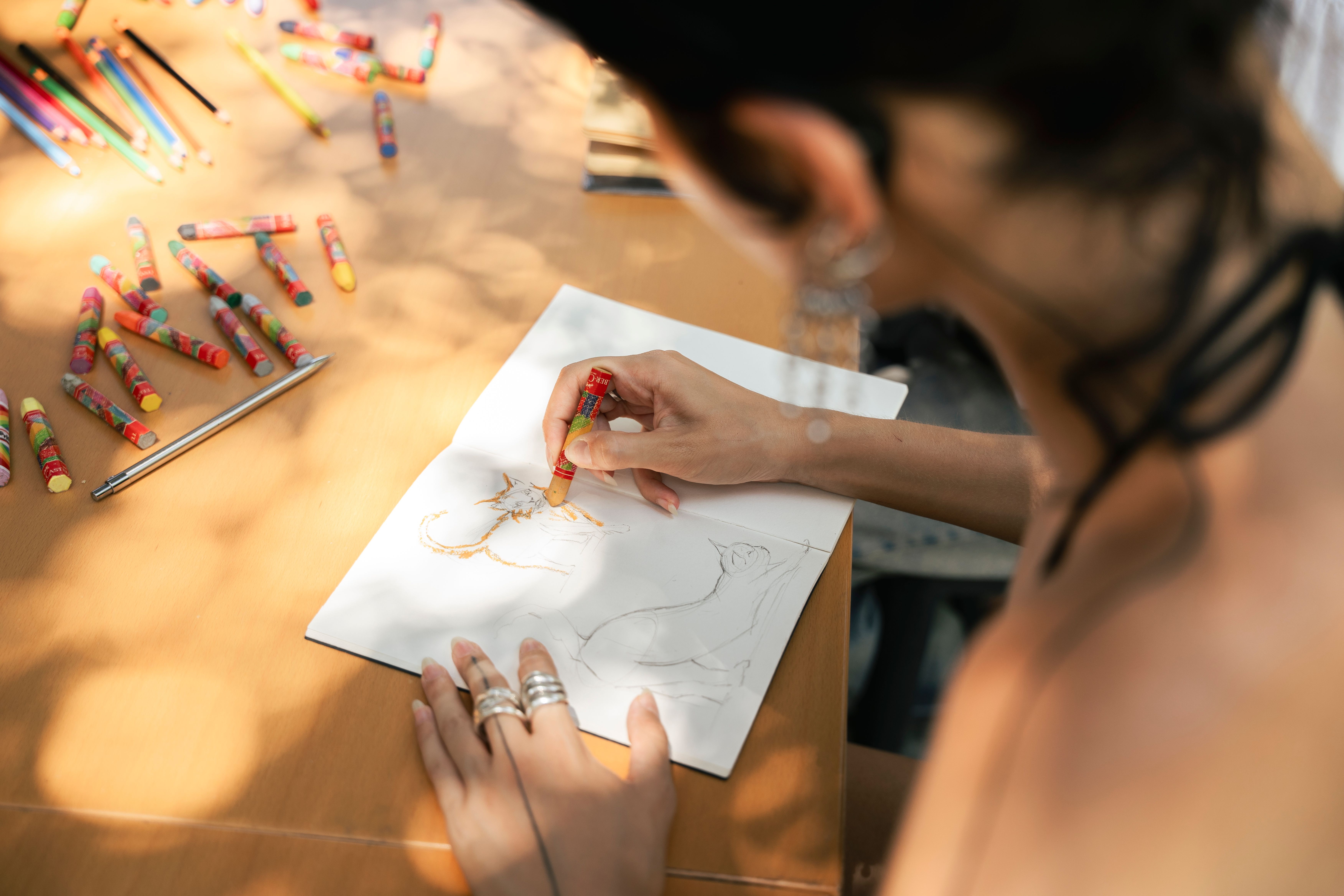 Un artiste dessine un chat avec des crayons sur papier, entouré de fournitures d'art colorées.