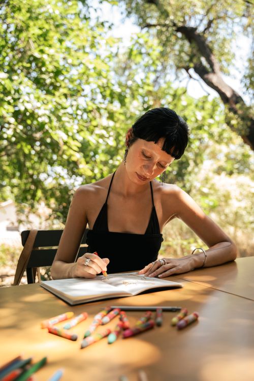 Free A woman artistically sketching in a serene outdoor garden setting during summer daylight. Stock Photo