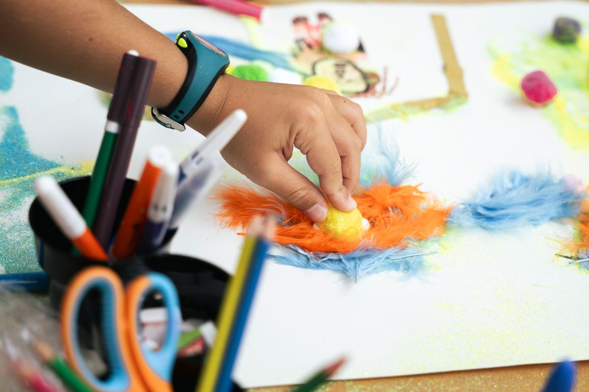 Child's hand creating colorful art with feathers and markers for a bookmark craft