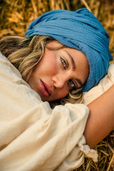 Close-up portrait of a woman with a blue headscarf lying on straw, showcasing natural beauty and serene expression.