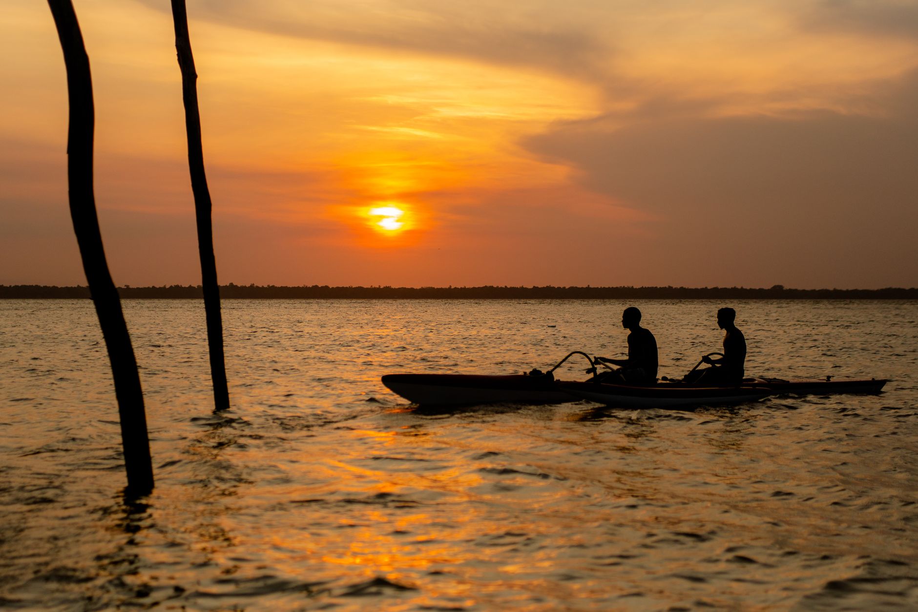 Silhouettes of two people kayaking on the Amazon River at sunset near Belém, Brazil.
