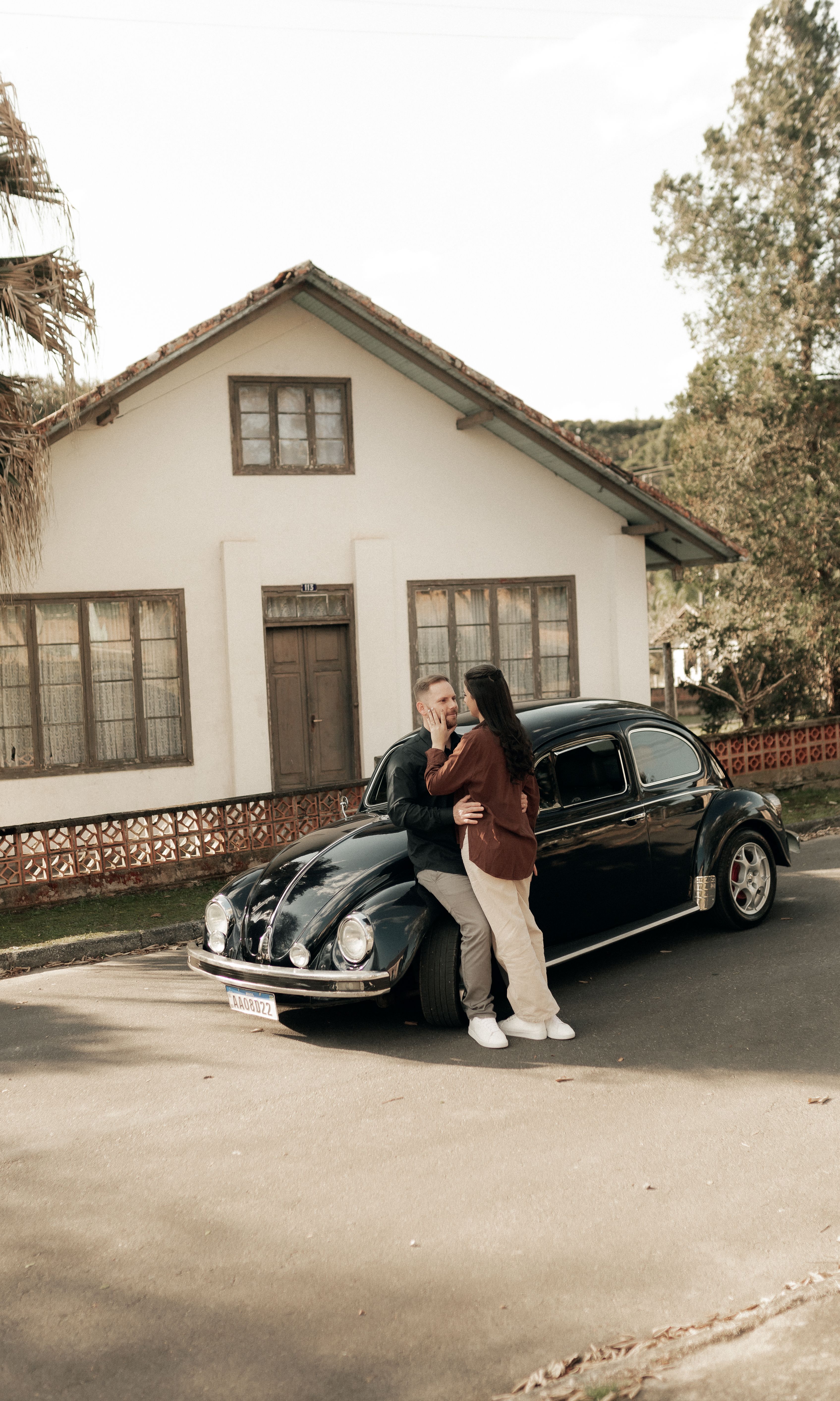 A loving couple embraces by a classic car in a peaceful suburban setting, evoking nostalgia.