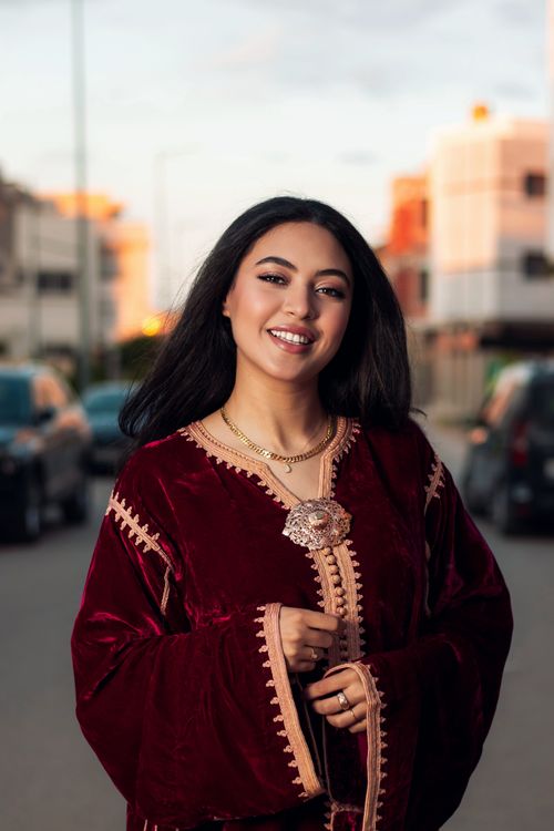 Free Elegant woman in a red velvet dress smiling on a street during sunset. Stock Photo