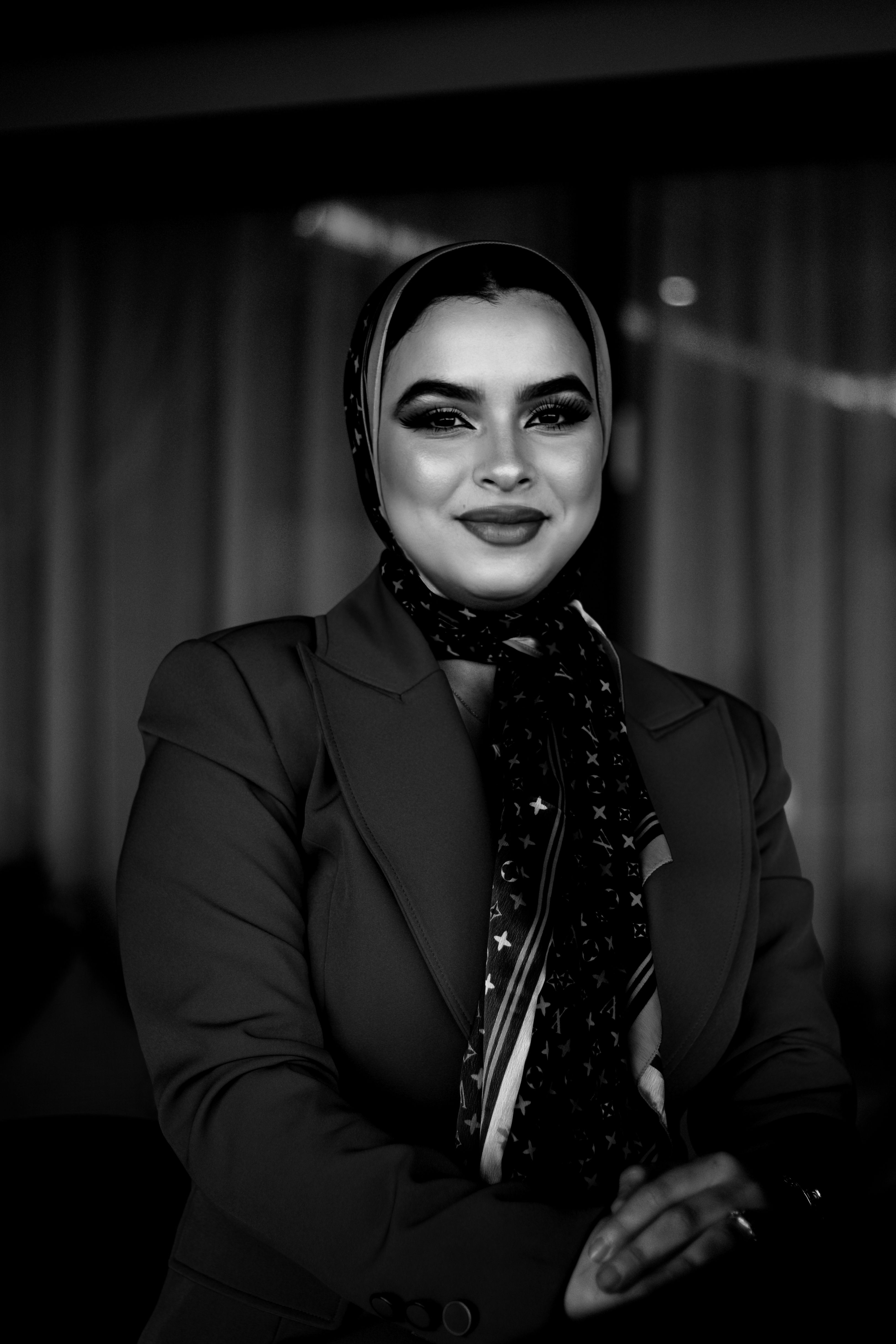 Captivating black and white portrait of a smiling woman in elegant attire, exuding confidence and charm.