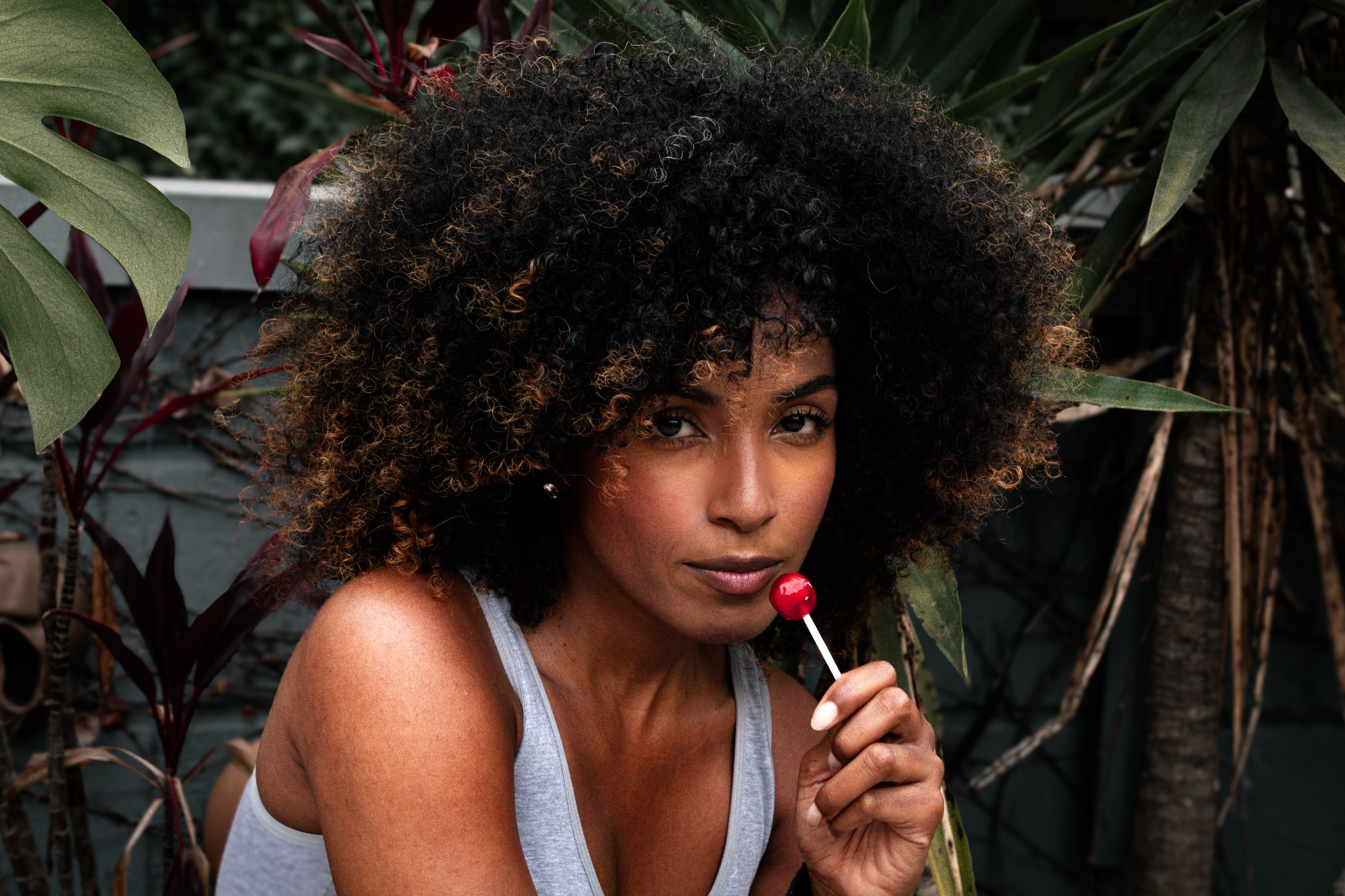 A confident woman with afro-textured hair enjoying a lollipop outdoors.