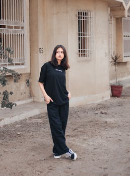 Woman poses stylishly in black streetwear on a Karachi street, exuding modern urban vibes.