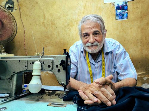 Free Experienced tailor sitting in workshop beside sewing machine, ready to sew clothing. Stock Photo