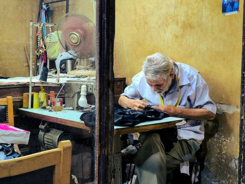 Free Elderly tailor concentrating on sewing in a small workshop with vintage decor. Stock Photo