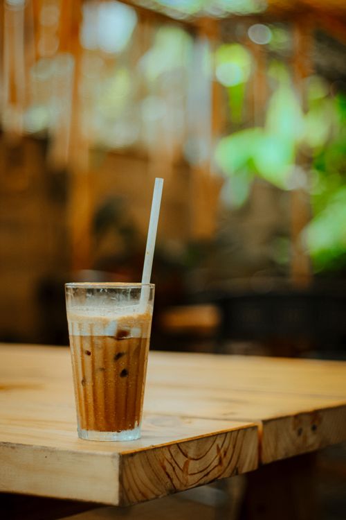 Free Refreshing iced coffee in a glass with straw on a wooden table outdoors. Stock Photo