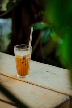 Refreshing glass of iced coffee with straw on a wooden table in a lush outdoor setting.