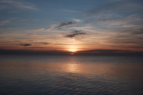 Free A beautiful sunset casting warm hues over tranquil ocean waters, creating a peaceful scene. Stock Photo