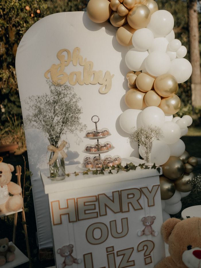 Gender reveal setup with gold and white balloons and teddy bears