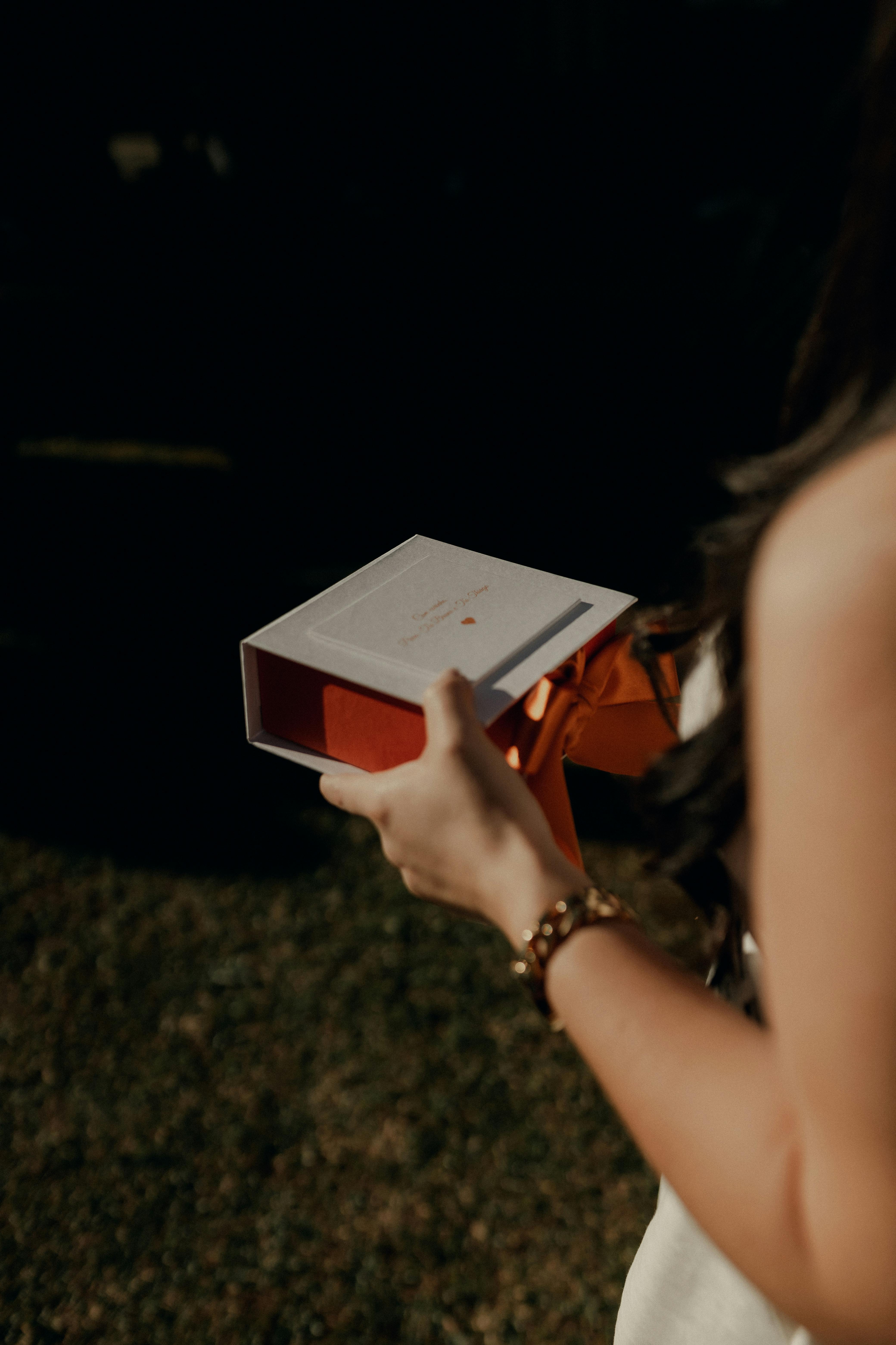 grátis Uma mulher segurando uma caixa de presente aberta com interior vermelho ao ar livre, criando um momento de expectativa. Foto profissional