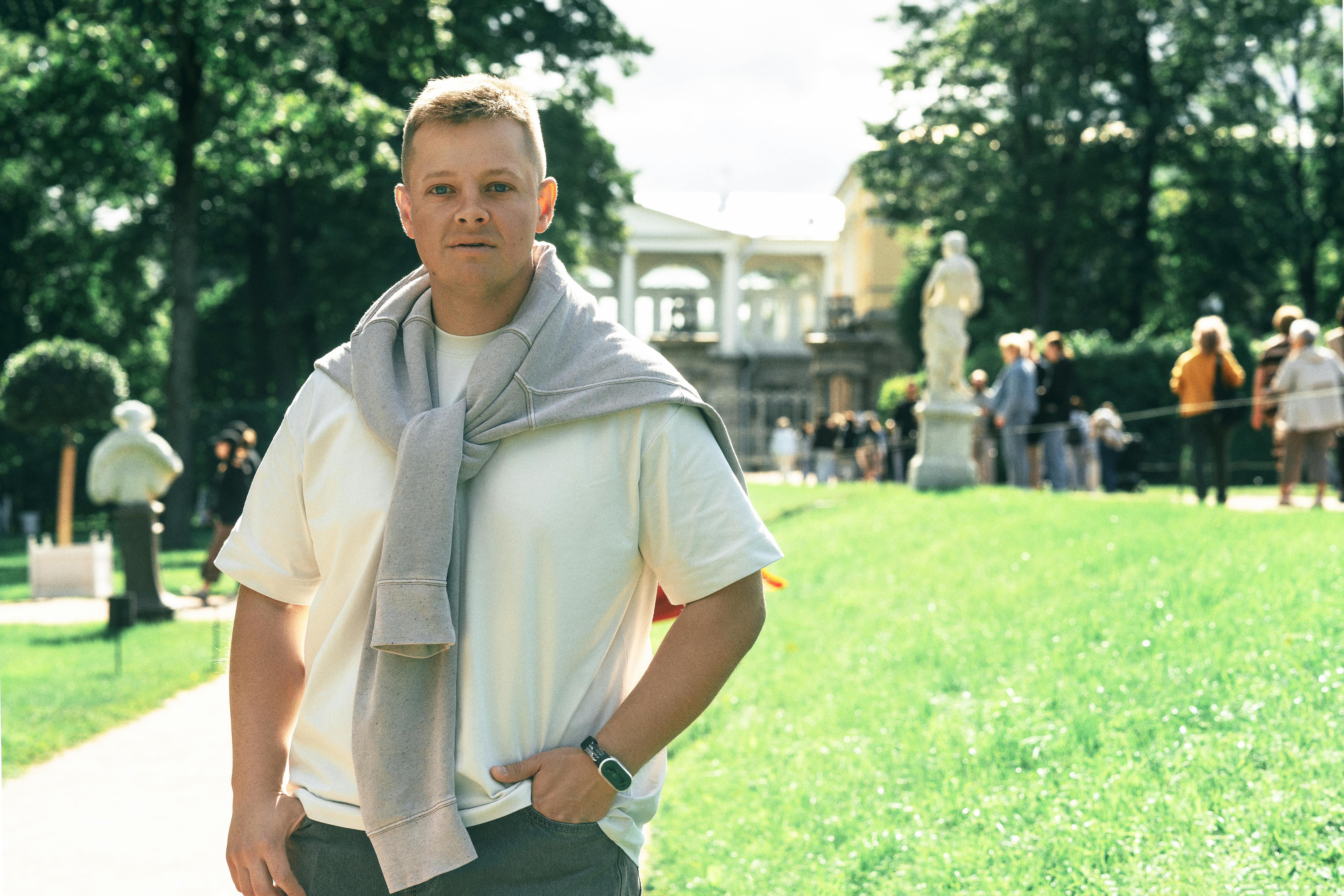 Portrait of a man enjoying a sunny day in a green park with statues.