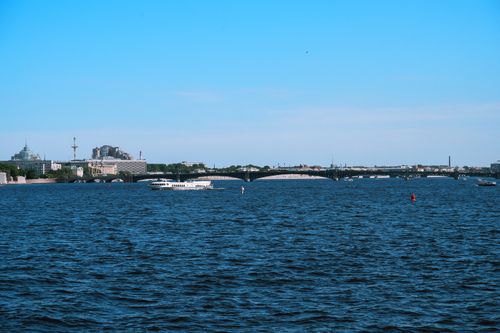 Free A tranquil view of a city skyline over a vast river with boats under a clear blue sky. Stock Photo