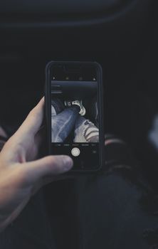 Smartphone capturing a photo of jeans and sneakers held in hand.