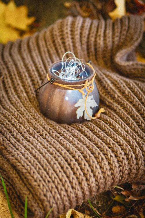 Free Artistic autumn setting featuring a knitted blanket and decorative lantern with fairy lights. Stock Photo