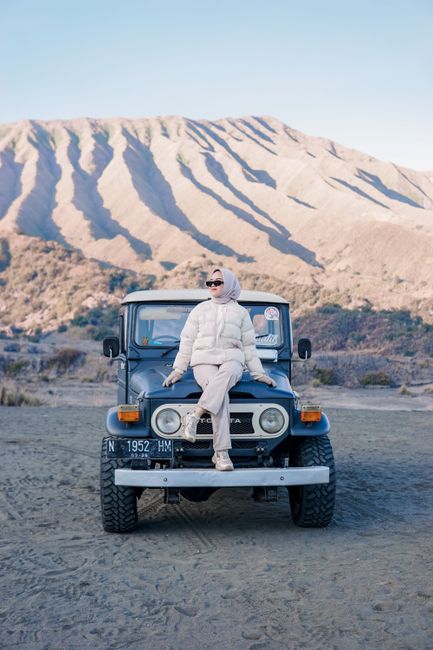 Adult woman in stylish outfit sits on a Jeep at Mount Bromo, showcasing travel adventure and style.