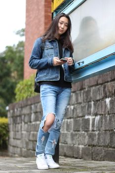 一位穿着牛仔服的年轻女子靠在城市街道的户外，使用着智能手机