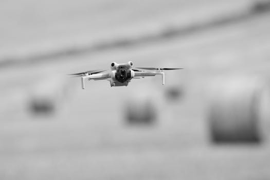 Black and white image of a drone flying over rural fields with hay bales in Gränna, Sweden.