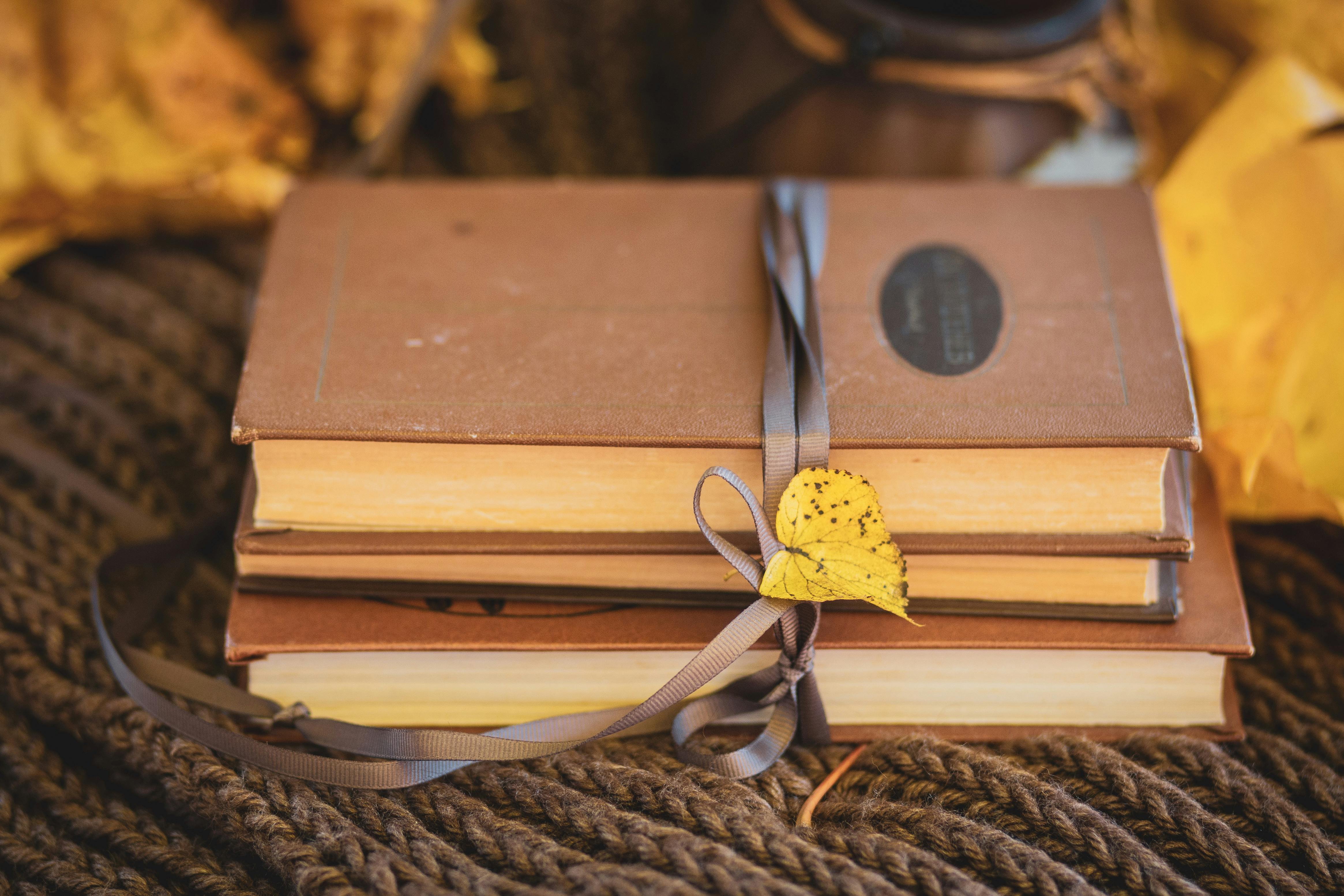 Stack of vintage books tied with ribbon and decorated with autumn leaves.