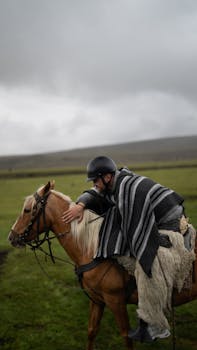 Man wearing a striped poncho riding a horse on a cloudy day in an open field.
