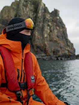 Man bundled in warm gear exploring Antarctica with rocky cliffs in the background.