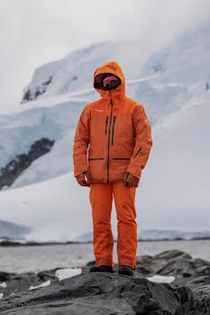 Explorer in orange gear stands on icy rocks in Antarctica.