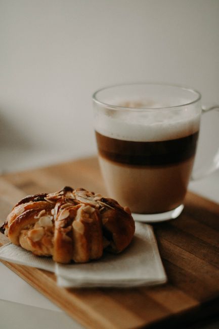 Tasty almond pastry pair with a creamy latte on a wooden board, ideal for breakfast.