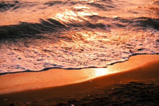 Captivating image of waves reflecting golden sunset hues, touching a tranquil sandy shore.