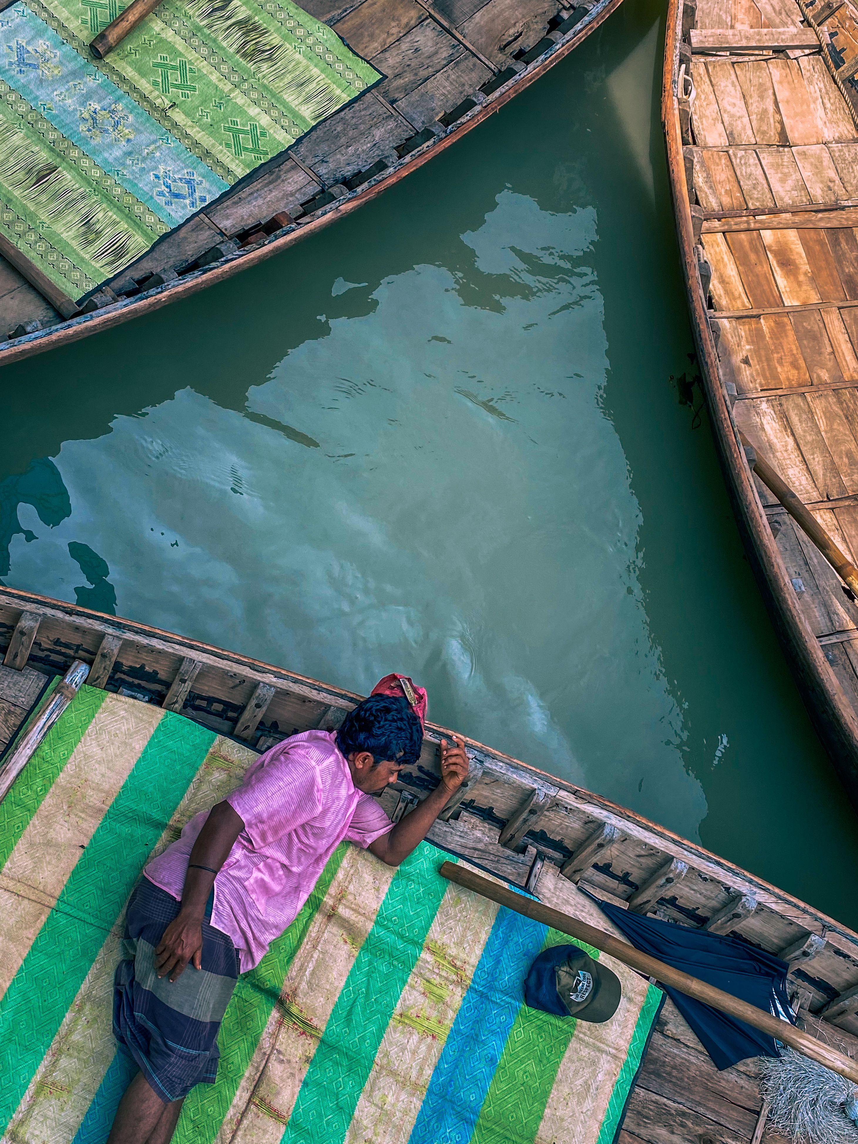 A man in a pink shirt rests on a boat, surrounded by calm water.