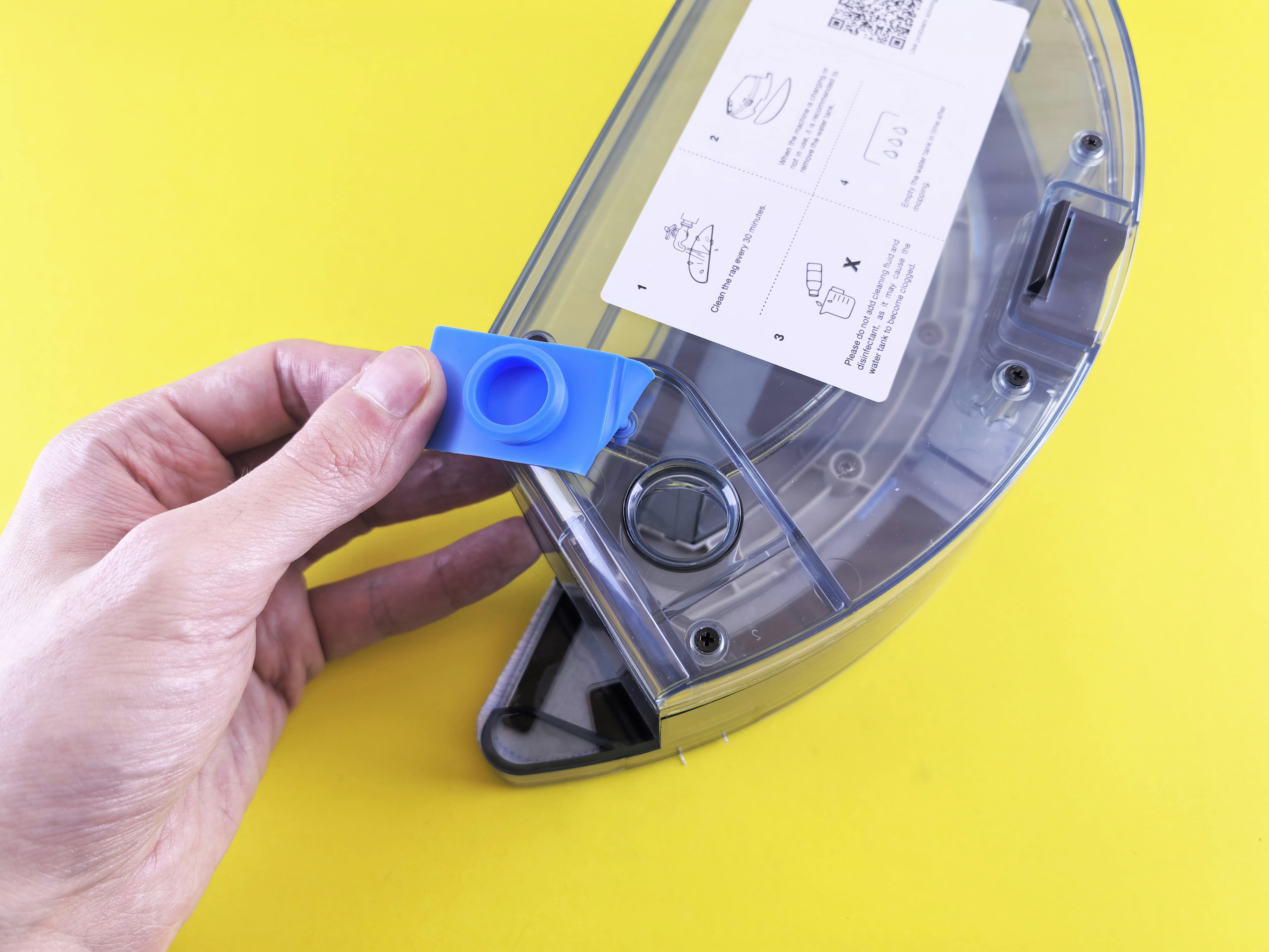 Close-up of a person holding a vacuum cleaner water tank with a yellow background.
