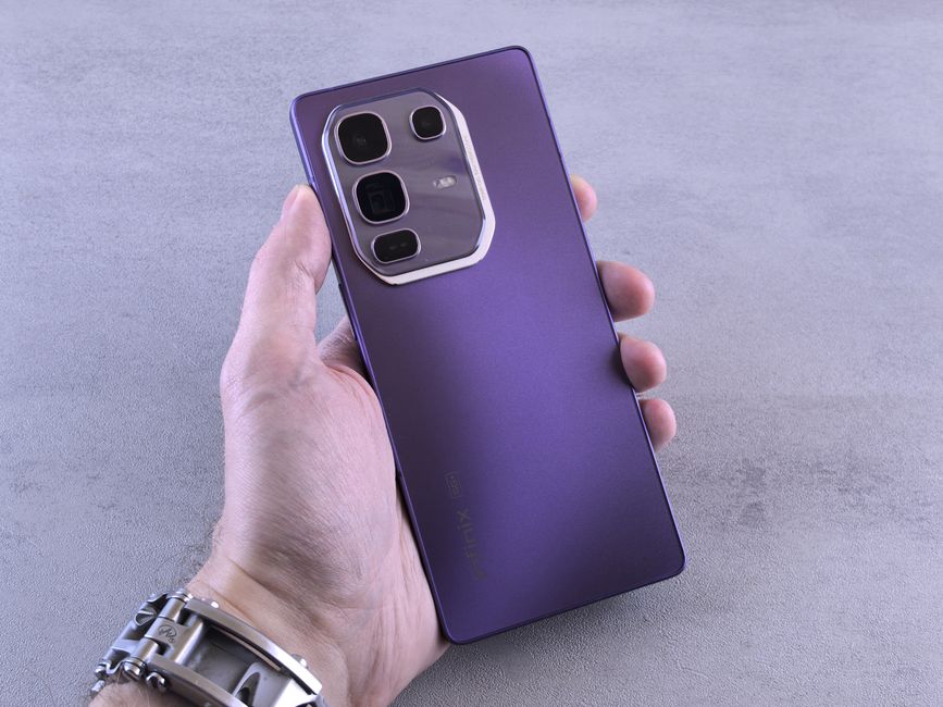 A person holds a sleek purple smartphone with multiple cameras on a gray surface.