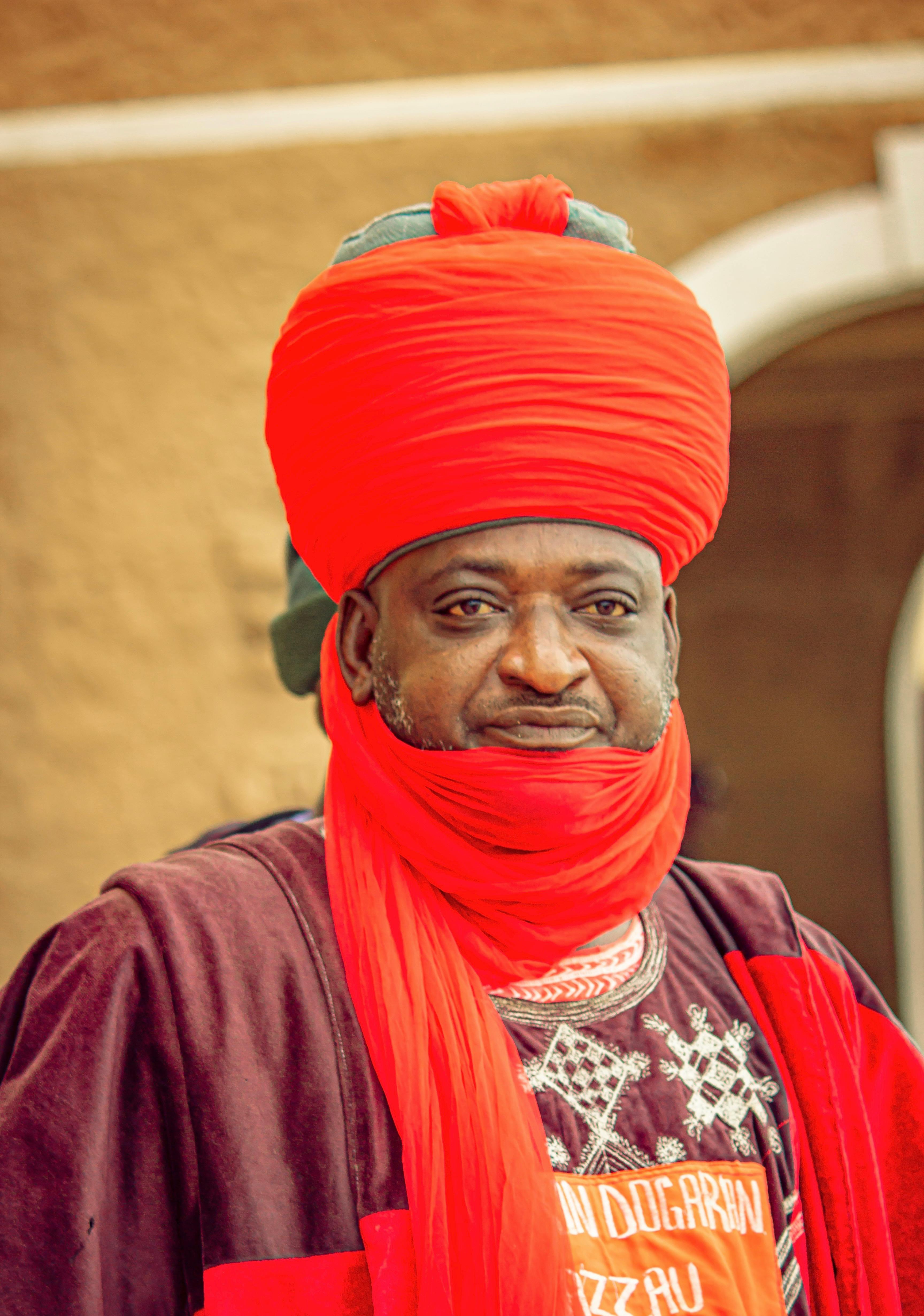 Adult man wearing traditional red turban and robes during cultural celebration.