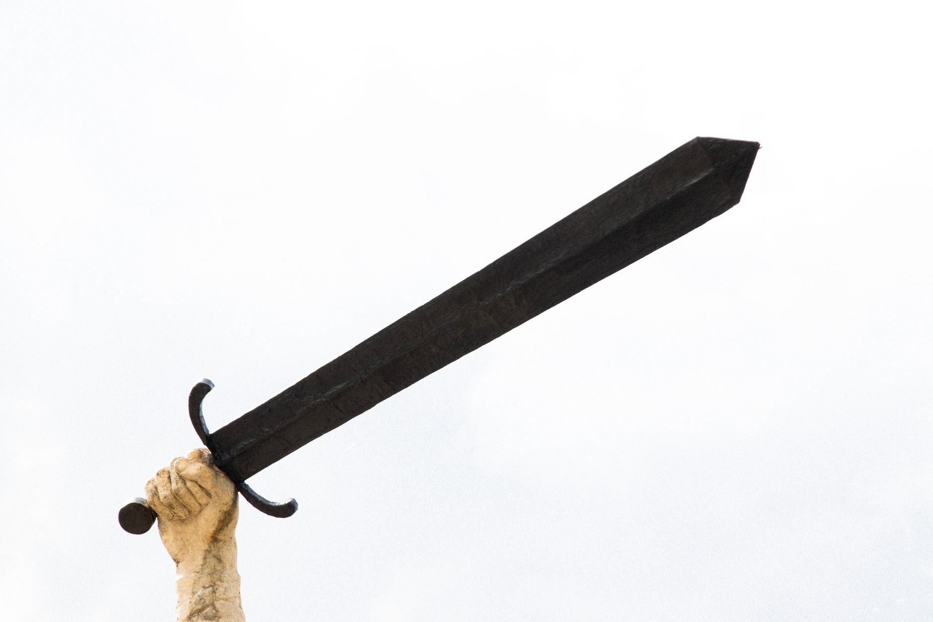 A stone sculpture hand holding a large sword against a bright sky, symbolizing power and strength.