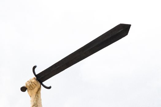 A stone sculpture hand holding a large sword against a bright sky, symbolizing power and strength.