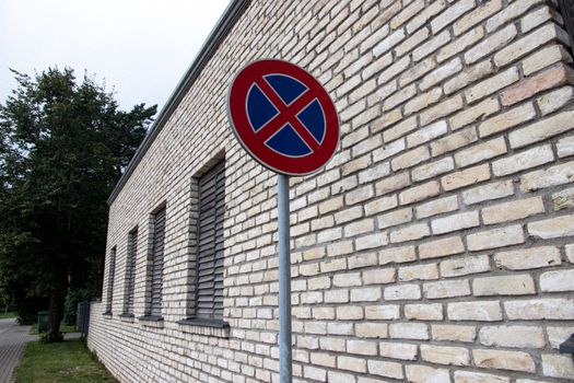 A brick building with a no parking sign on an urban street corner, featuring a tree-lined sidewalk.