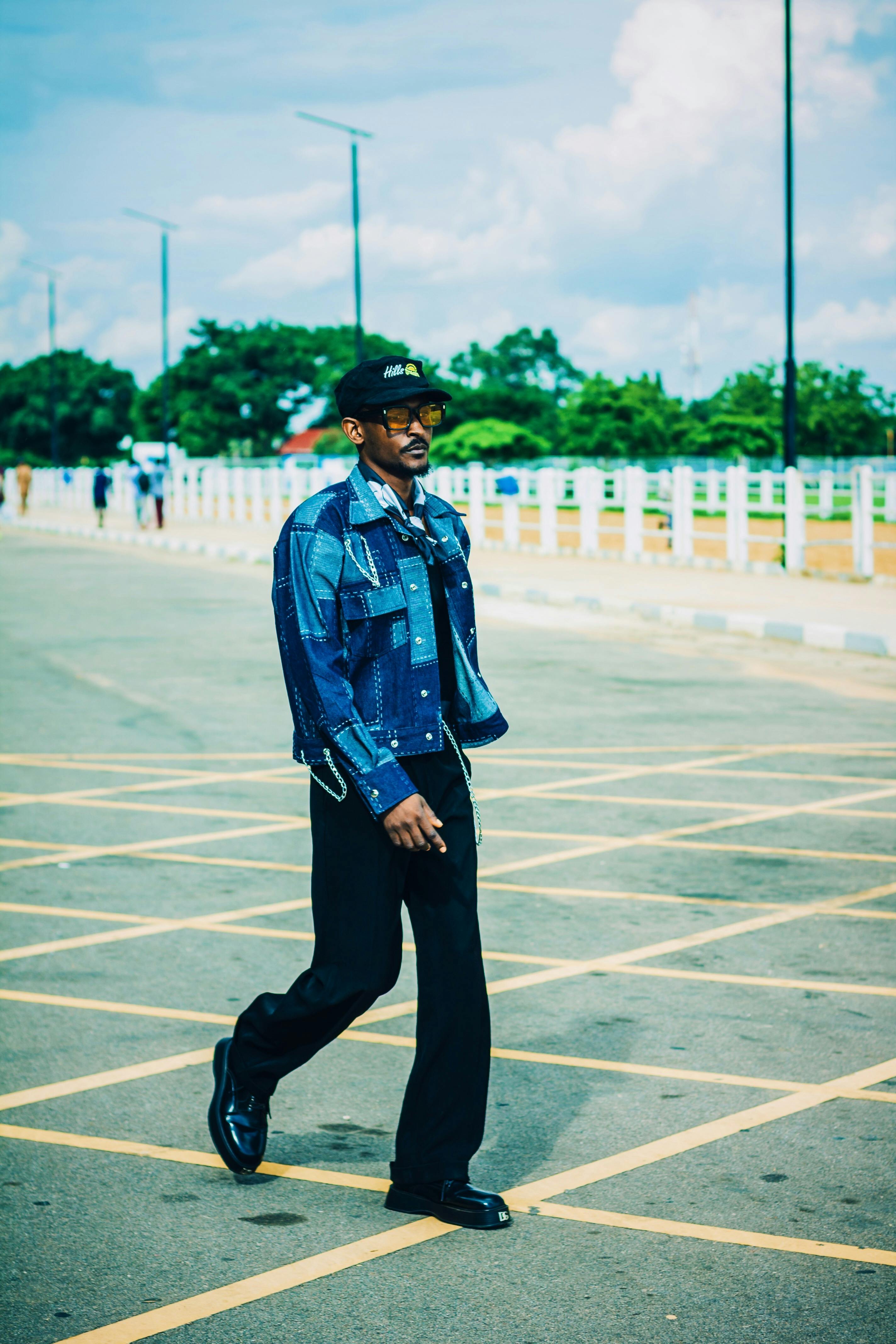 grátis Homem elegante em traje jeans casual caminhando com confiança ao ar livre em um dia ensolarado. Foto profissional