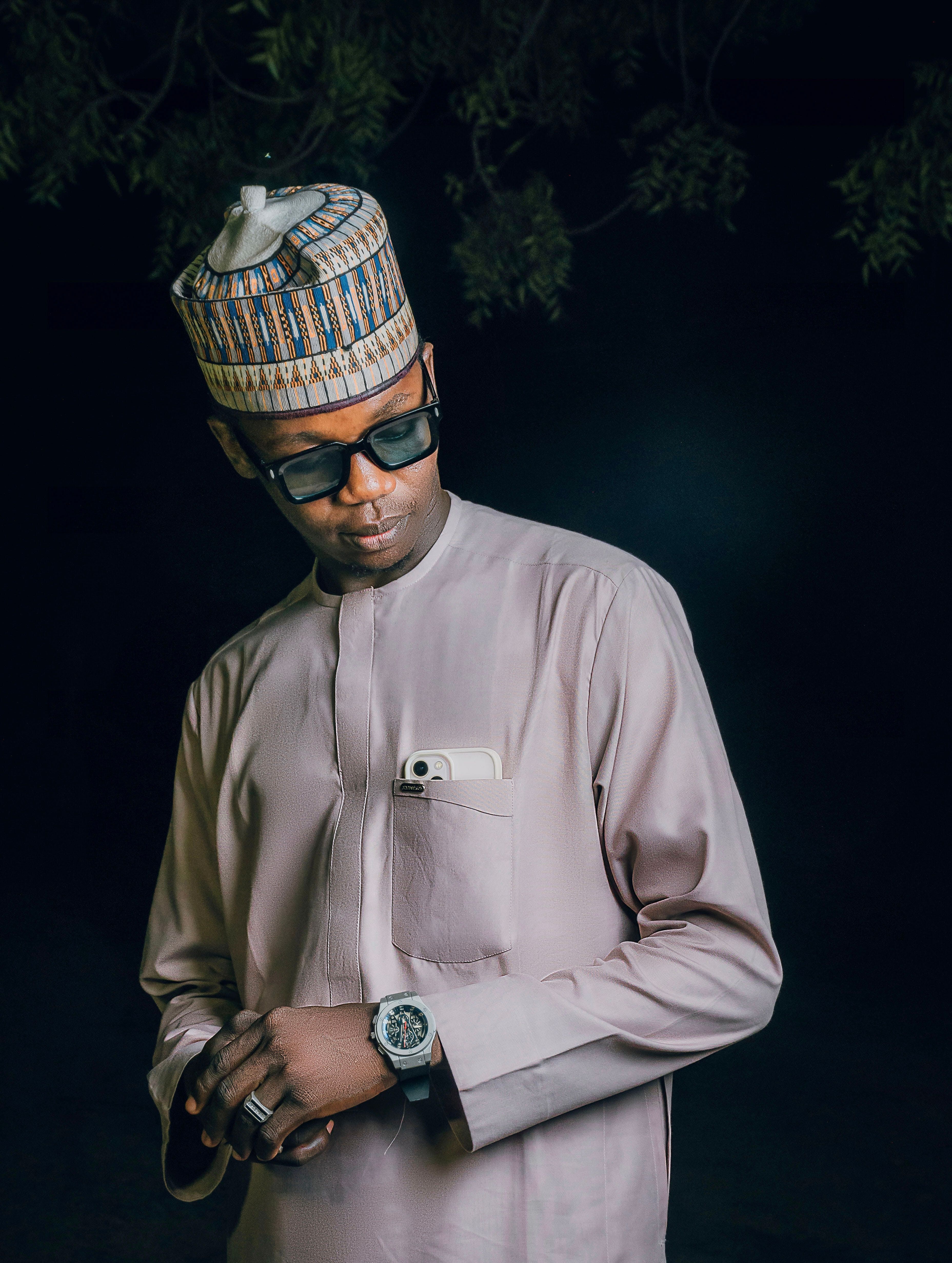 A poised man wearing traditional Nigerian attire with sunglasses and a watch.