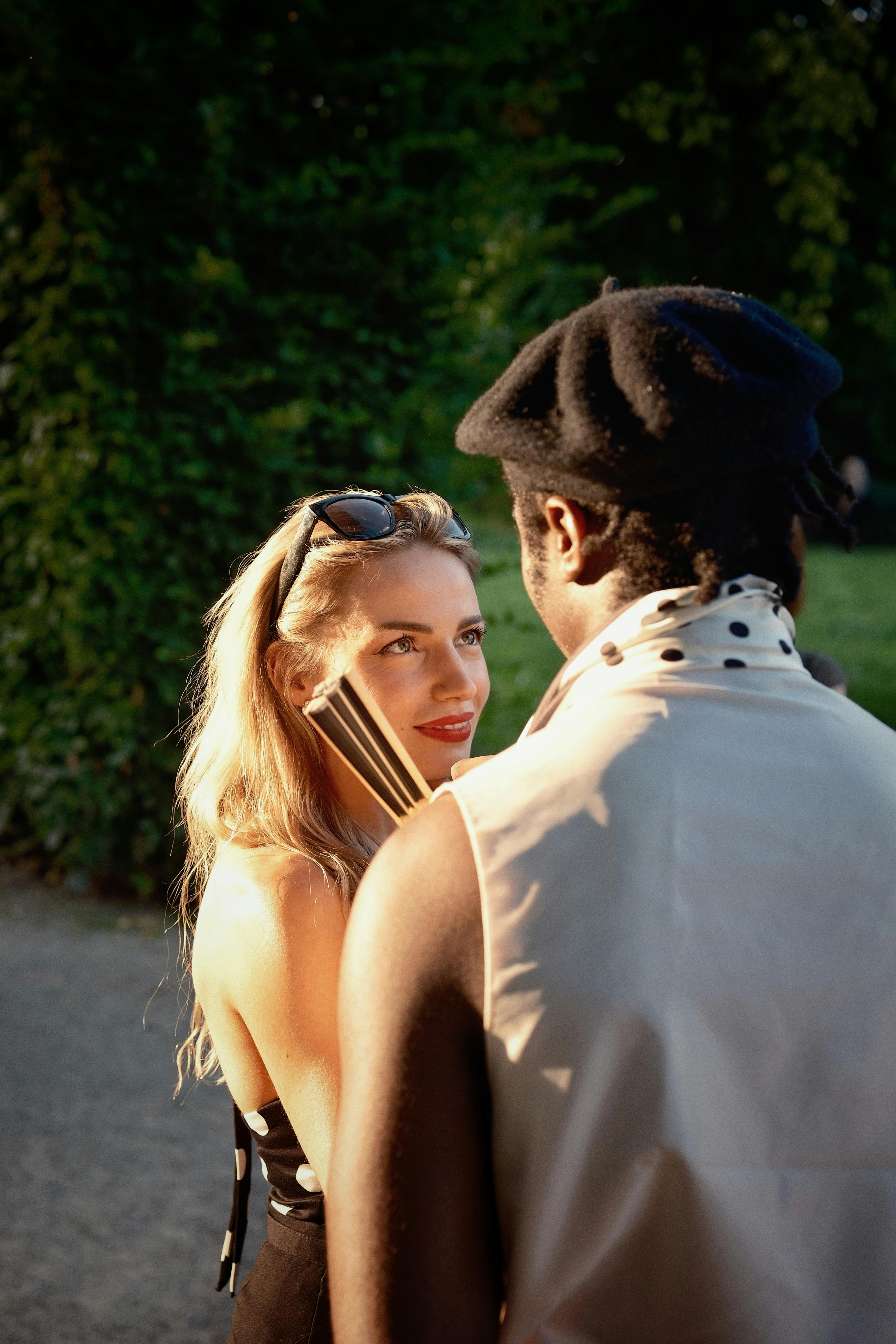 A cheerful couple enjoys a conversation under warm sunlight in a lush park.