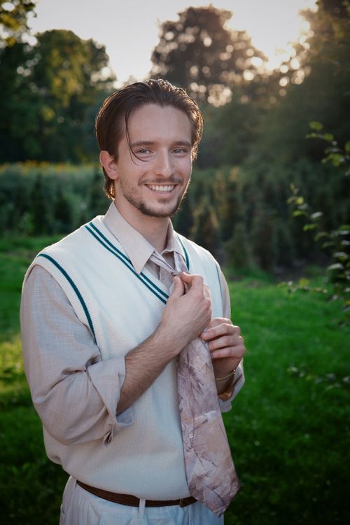 Free A cheerful young man adjusts his tie in a sunlit garden setting, exuding a relaxed and vibrant vibe. Stock Photo