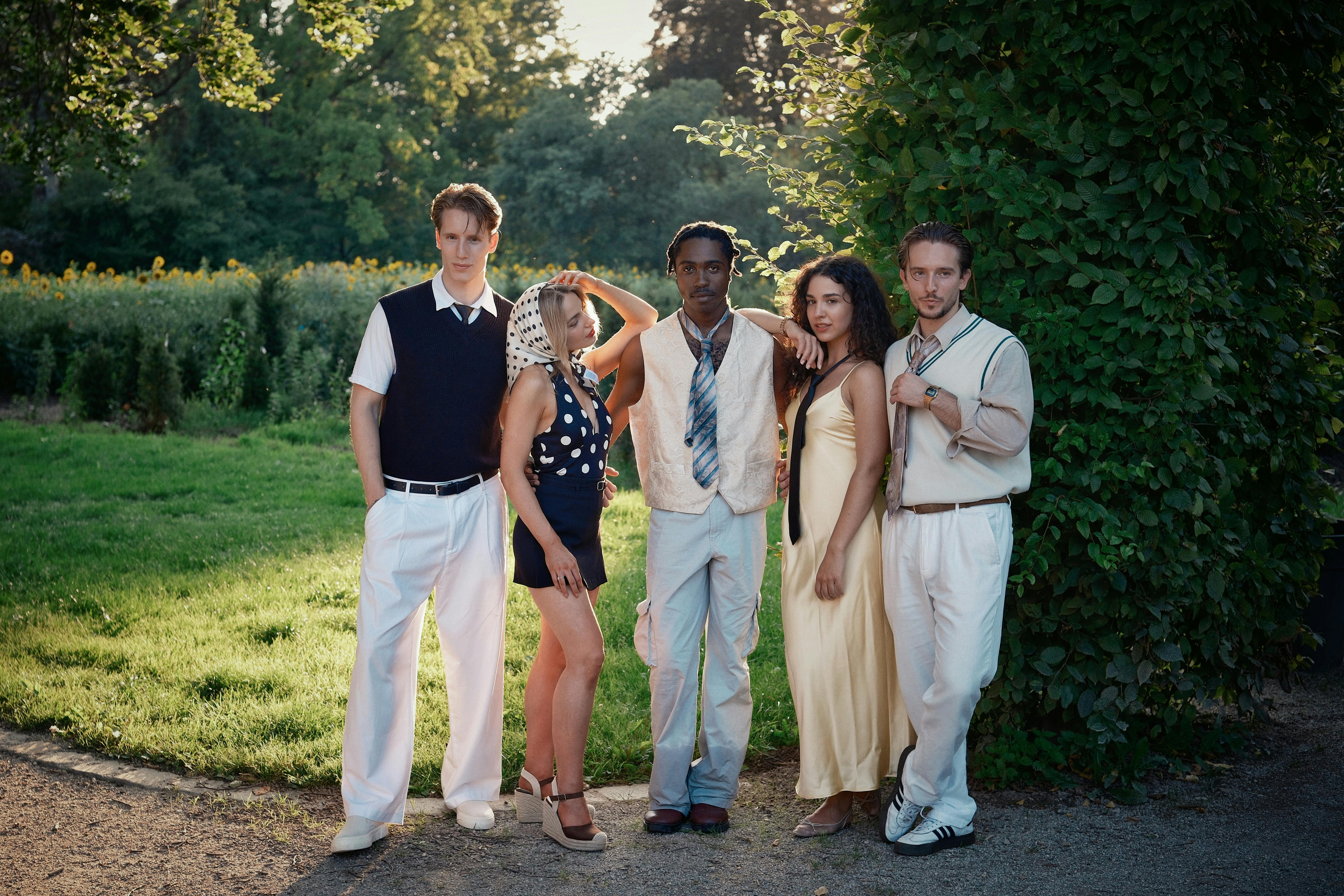 Five stylish young adults posing in a summer park, exuding modern fashion and confidence.