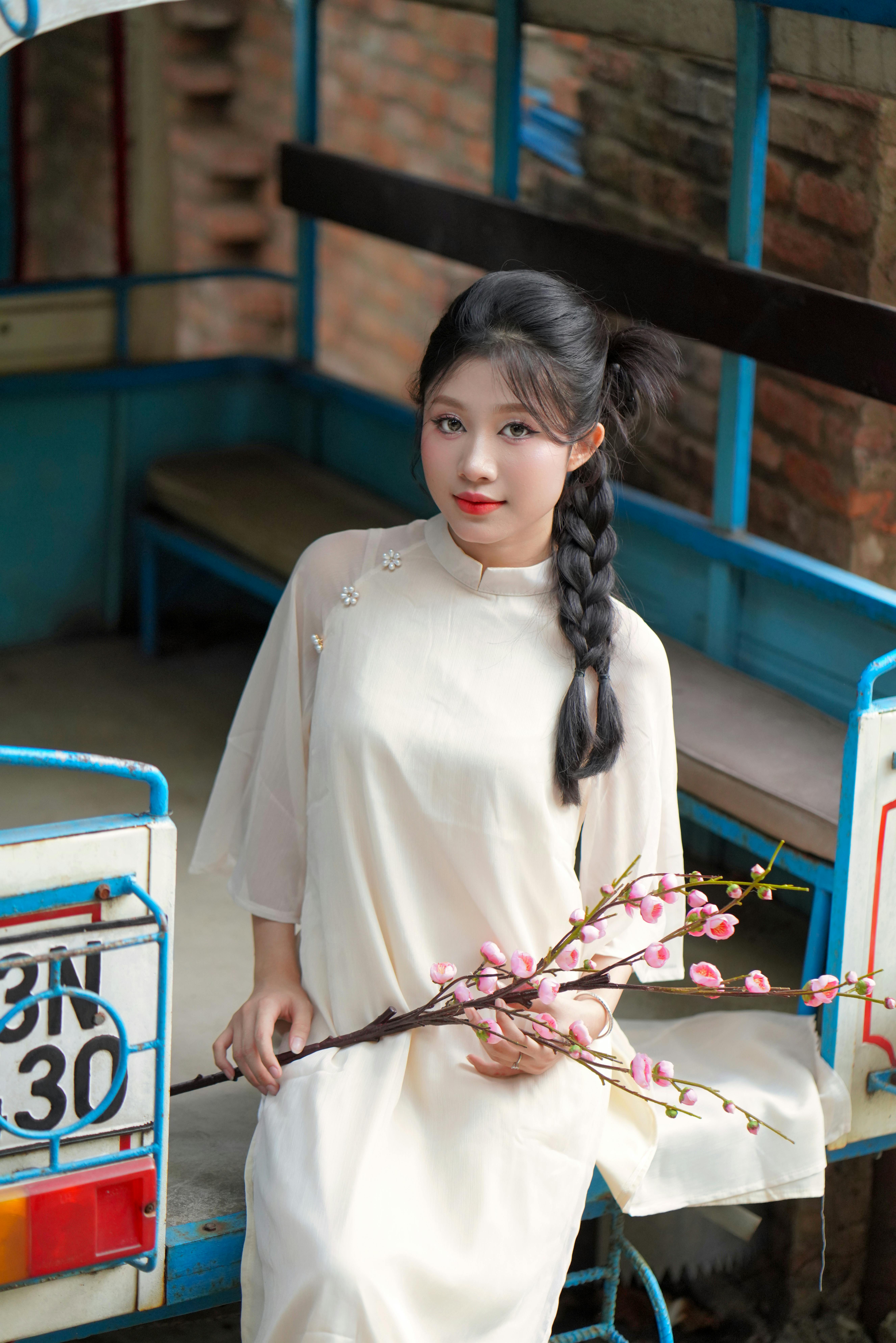 Portrait of a young woman holding peach blossom, wearing traditional dress, sitting in a rickshaw.